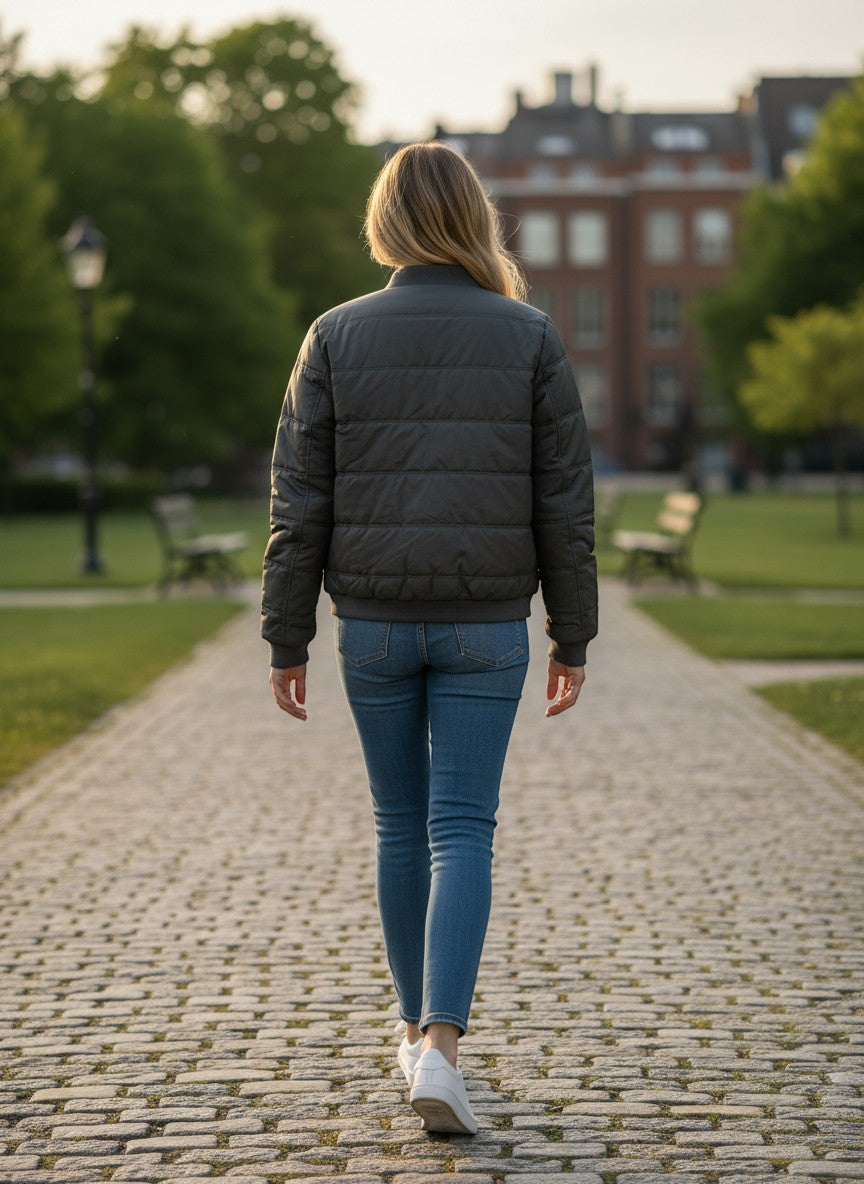 Throwback Rack Levi's dark green lightweight puffer jacket worn by a woman in blue jeans and white sneakers walking away.
