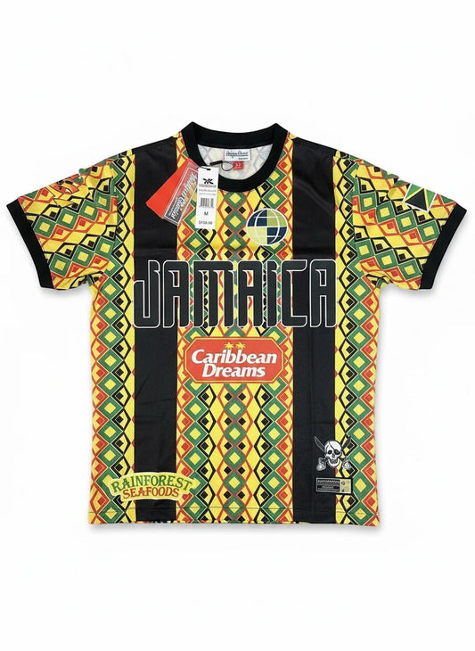 Throwback Rack Jamaica 1990 World Cup retro soccer jersey with geometric pattern in green, yellow, red, and black. Features "JAMAICA" text and sponsor logos.